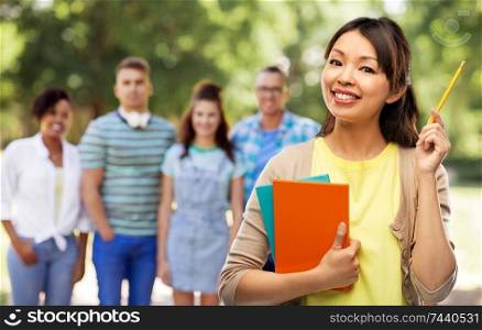 education, high school and knowledge concept - asian student woman with books and pencil over group of people in summer park background. asian student woman with books and pencil