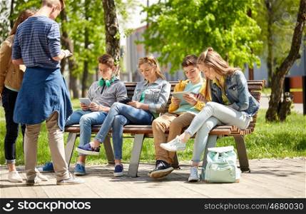education, high school and people concept - group of happy teenage students with tablet pc computers sitting on bench at campus yard
