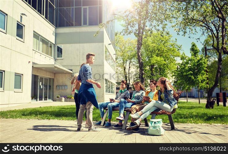 education, high school and people concept - group of happy teenage students with tablet pc computers sitting on bench at campus yard. teenage students with tablet pc at school yard. teenage students with tablet pc at school yard