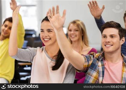 education, high school and people concept - group of smiling students raising hand in lecture hall. group of smiling students in lecture hall