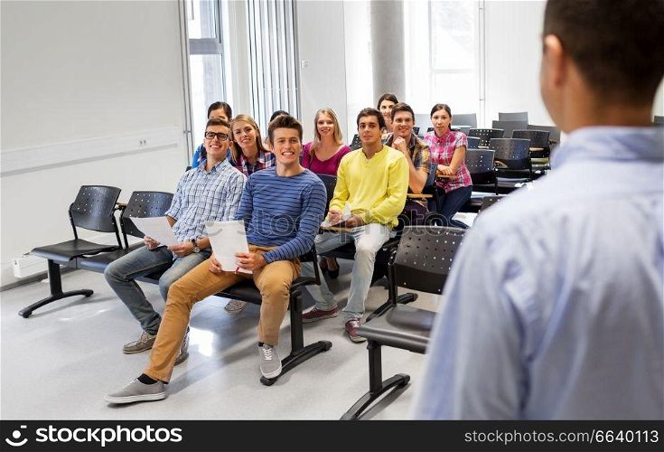 education, high school and people concept - group of smiling students with papers or tests and teacher at lecture hall. group of students and teacher at lecture hall