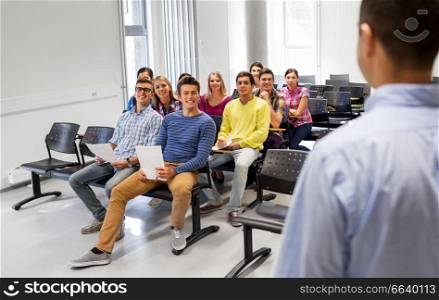 education, high school and people concept - group of smiling students with papers or tests and teacher at lecture hall. group of students and teacher at lecture hall