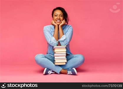 education, high school and people concept - happy african american young student woman with books sitting on floor over pink background. happy african american student woman with books