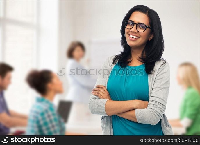 education, high school and people concept - happy smiling young indian woman or teacher in glasses over classroom background. happy smiling young indian woman in glasses