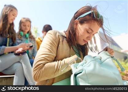 education, high school and people concept - happy teenage student girl looking for something in her backpack outdoors