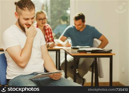 Education, high school, digital online learning concept - student boy with tablet pc computer sitting in front of students her group mates in classroom. Student boy with tablet in front of her classmates
