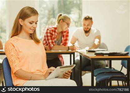 Education, high school, digital online learning concept - student girl with tablet pc computer sitting in front of students her group mates in classroom. Student girl with tablet in front of her classmates