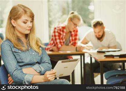 Education, high school, digital online learning concept - student girl with tablet pc computer sitting in front of students her group mates in classroom. Student girl with tablet in front of her classmates