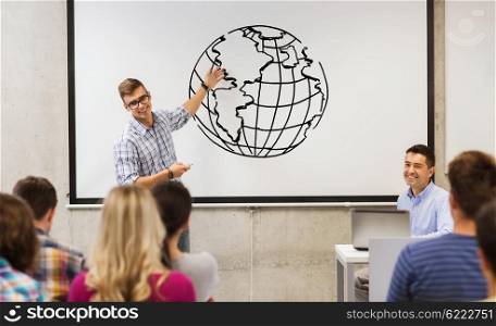 education, high school, geography and people concept - student standing with remote control in front of teacher and classmates in classroom and showing earth globe drawing on white board in classroom