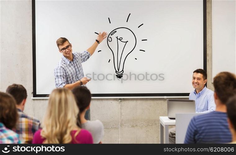 education, high school, idea and people concept - student standing with remote control in front of teacher and classmates in classroom and showing light bulb on white board in classroom