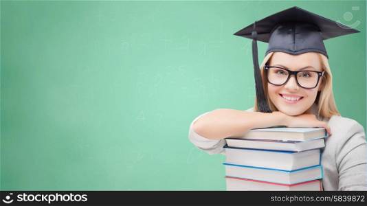 education, high school, knowledge, and people concept - picture of happy student girl or woman in trencher cap with stack of books over green chalk board background