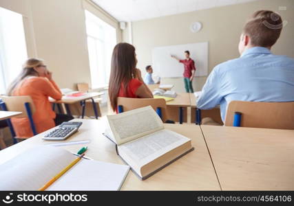 education, high school, learning and people concept - close up of notebook with pencil, book and calculator on desk