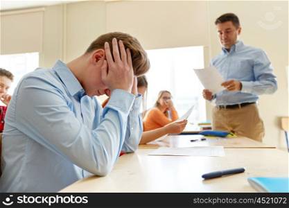 education, high school, learning and people concept - upset student boy and teacher with bad test results in classroom