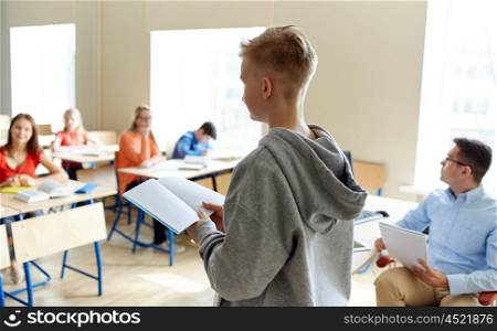 education, high school, learning, examination and people concept - student boy with notebook and teacher in classroom
