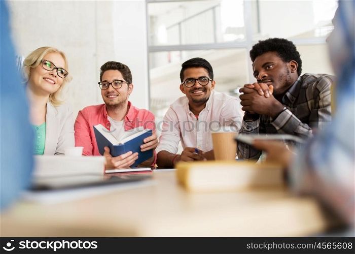 education, high school, learning, people and technology concept - group of international students sitting at table with coffee and books and talking at university
