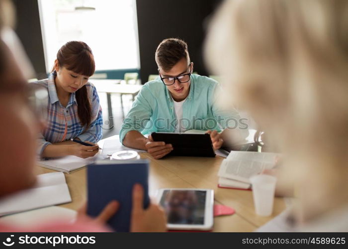 education, high school, learning, people and technology concept - group of international students sitting at table with tablet pc computers, books and notebooks at university