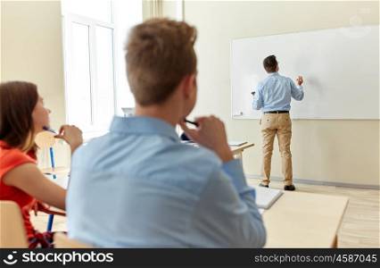 education, high school, learning, teaching and people concept - teacher standing in front of students and writing something on white board in classroom