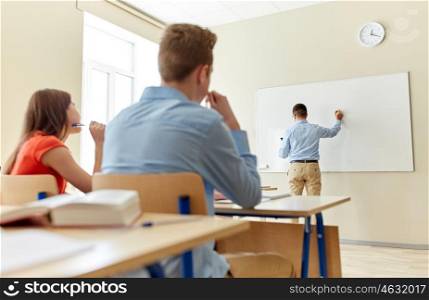 education, high school, learning, teaching and people concept - teacher standing in front of students and writing something on white board in classroom