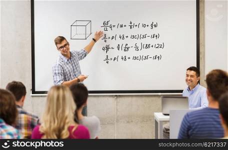 education, high school, mathematics and people concept - student standing with remote control in front of teacher and classmates and showing mathematical equalities on white board in classroom