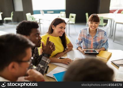 education, high school, people and technology concept - group of international students sitting at table with tablet pc computers, books and notebooks talking at university