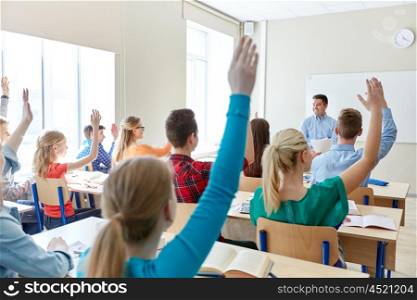 education, high school, teaching, learning and people concept - group of happy students raising hands and teacher in classroom