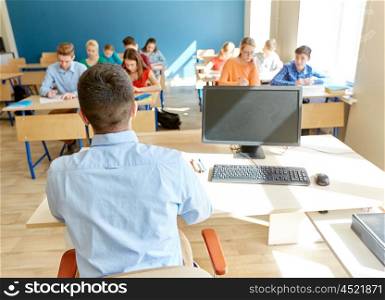 education, high school, teaching, technology and people concept - group of students writing test and teacher sitting at table with pc computer