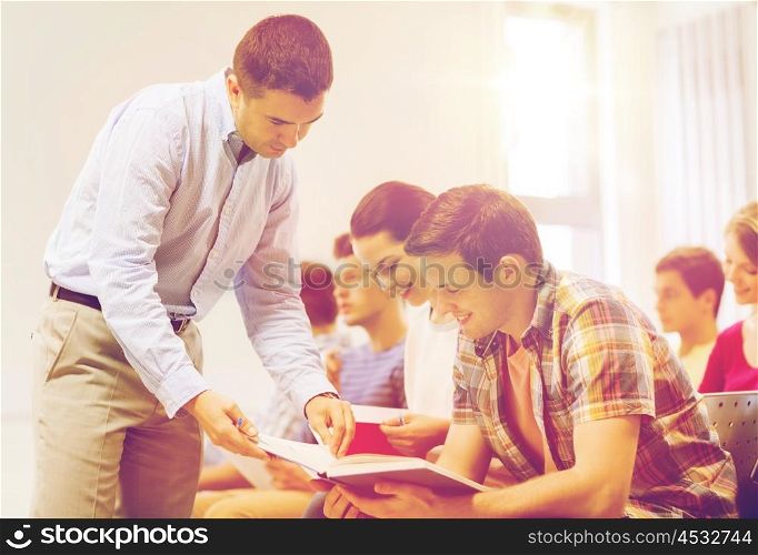 education, high school, teamwork and people concept - group of smiling students and teacher with books talking in classroom