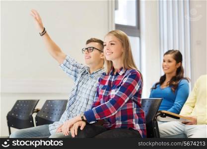 education, high school, teamwork and people concept - group of smiling students raising hand in lecture hall