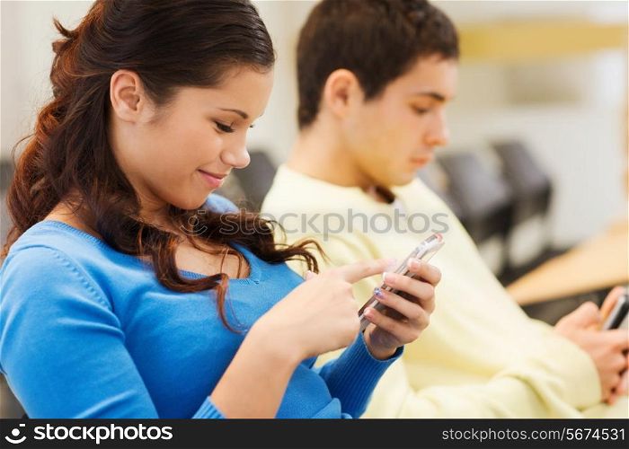 education, high school, teamwork and people concept - group of smiling students with smartphones in lecture hall