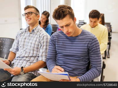 education, high school, teamwork and people concept - group of smiling students with notepads sitting in lecture hall