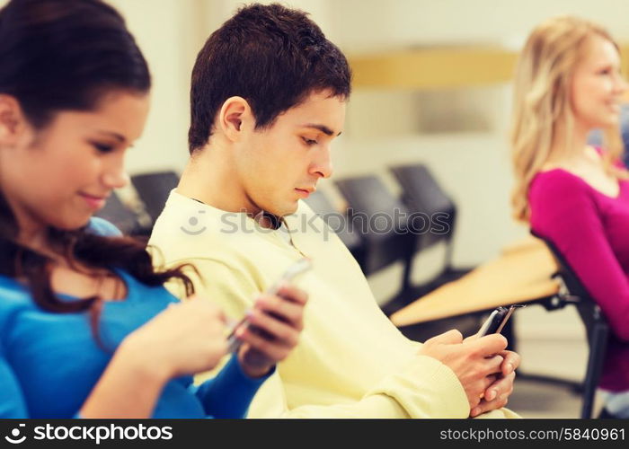 education, high school, teamwork and people concept - group of smiling students with smartphones in lecture hall