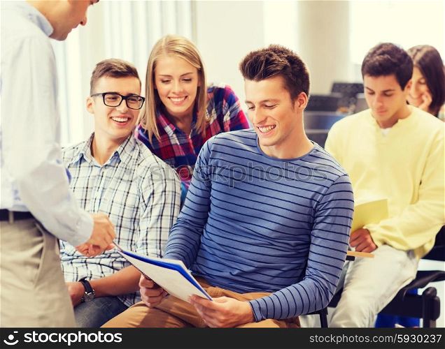 education, high school, teamwork and people concept - group of smiling students with notebooks and teacher talking in classroom
