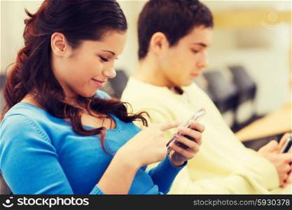 education, high school, teamwork and people concept - group of smiling students with smartphones in lecture hall