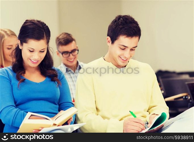 education, high school, teamwork and people concept - group of smiling students with notebooks and book sitting in lecture hall and writing