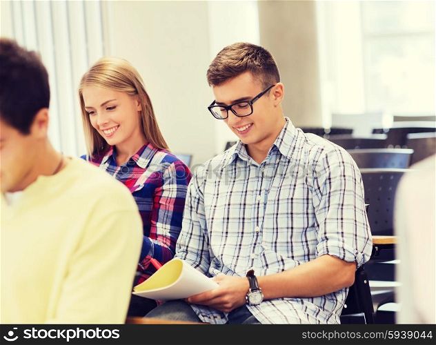 education, high school, teamwork and people concept - group of smiling students with notebook sitting in lecture hall and writing