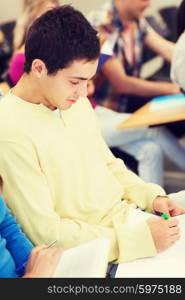 education, high school, teamwork and people concept - group of smiling students with notebooks and books writing in lecture hall