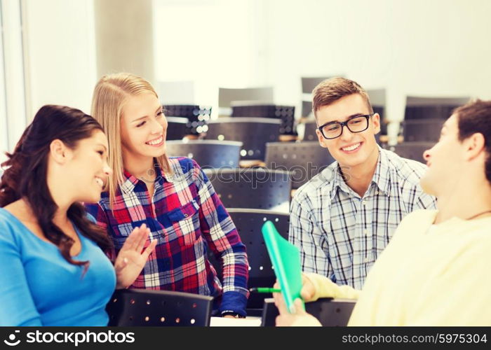 education, high school, teamwork and people concept - group of smiling students with notebook sitting in lecture hall and talking