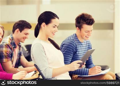 education, high school, teamwork and people concept - group of smiling students with tablet pc computer and notebooks sitting in lecture hall