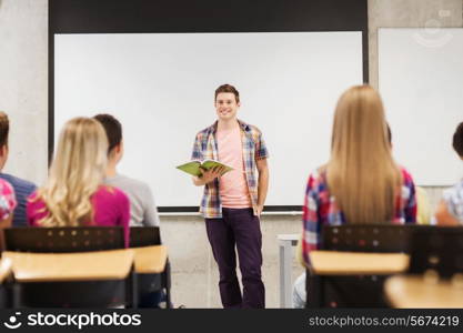 education, high school, teamwork and people concept - smiling student boy with notebook standing in front of students in classroom