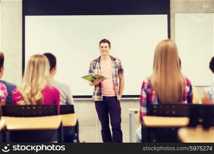 education, high school, teamwork and people concept - smiling student boy with notebook standing in front of students in classroom
