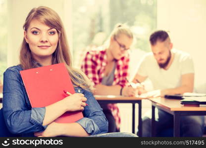 Education, high school, teamwork and people concept - smiling student girl with notebook sitting in front of students her group mates in classroom. Student girl in front of her mates in classroom