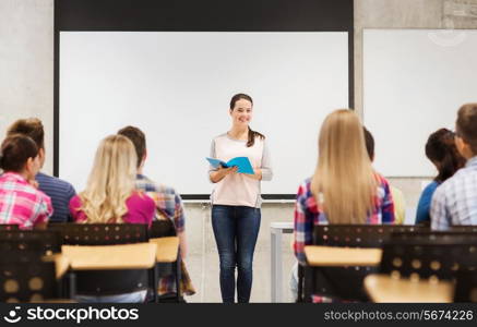 education, high school, teamwork and people concept - smiling student girl with notebook standing in front of students in classroom