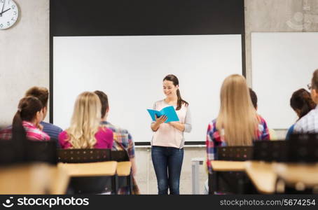 education, high school, teamwork and people concept - smiling student girl with notebook standing in front of students in classroom