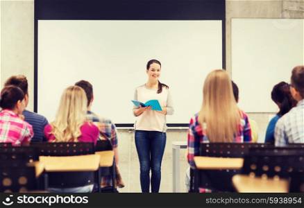 education, high school, teamwork and people concept - smiling student girl with notebook standing in front of students in classroom