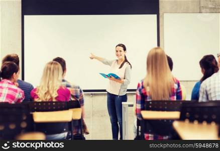 education, high school, teamwork and people concept - smiling student girl with notebook standing and pointing finger in front of students in classroom