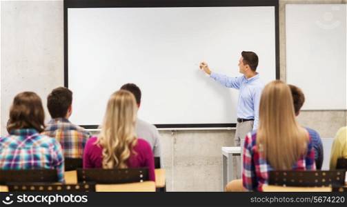 education, high school, teamwork and people concept - smiling teacher standing in front of students and writing something on white board in classroom