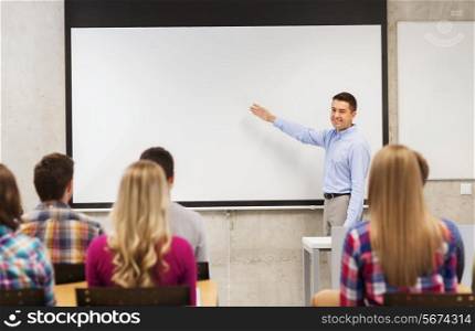 education, high school, teamwork and people concept - smiling teacher standing in front of students and showing something on white board in classroom