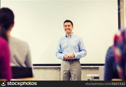 education, high school, teamwork and people concept - smiling teacher standing in front of white board and students in classroom