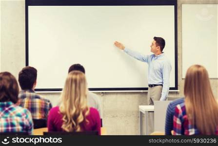 education, high school, teamwork and people concept - smiling teacher standing in front of students and showing something on white board in classroom