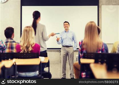 education, high school, teamwork and people concept - smiling teacher standing in front of white board and students in classroom